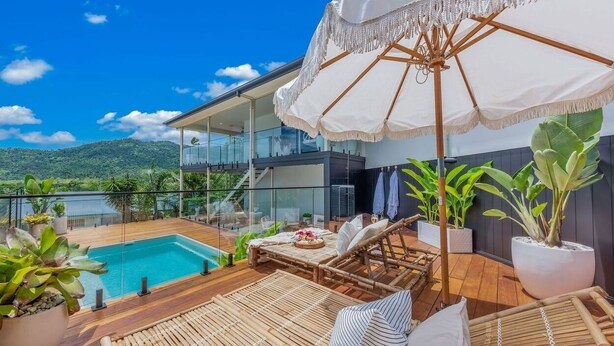 Una terraza moderna al aire libre con piscina, sillas de descanso y una sombrilla grande.
