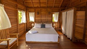 Ein Zimmer in einer Holzhütte mit einem Bett, zwei Nachttischen, einem Sessel und Vorhängen.