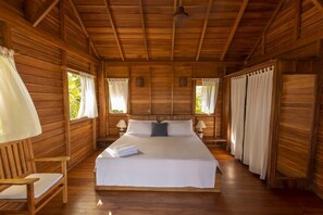 A wooden cabin room with a bed, two bedside tables, a chair, and curtains. - 3BR Ocean View Villa w/ Pool + Included Breakfast (Cobano)