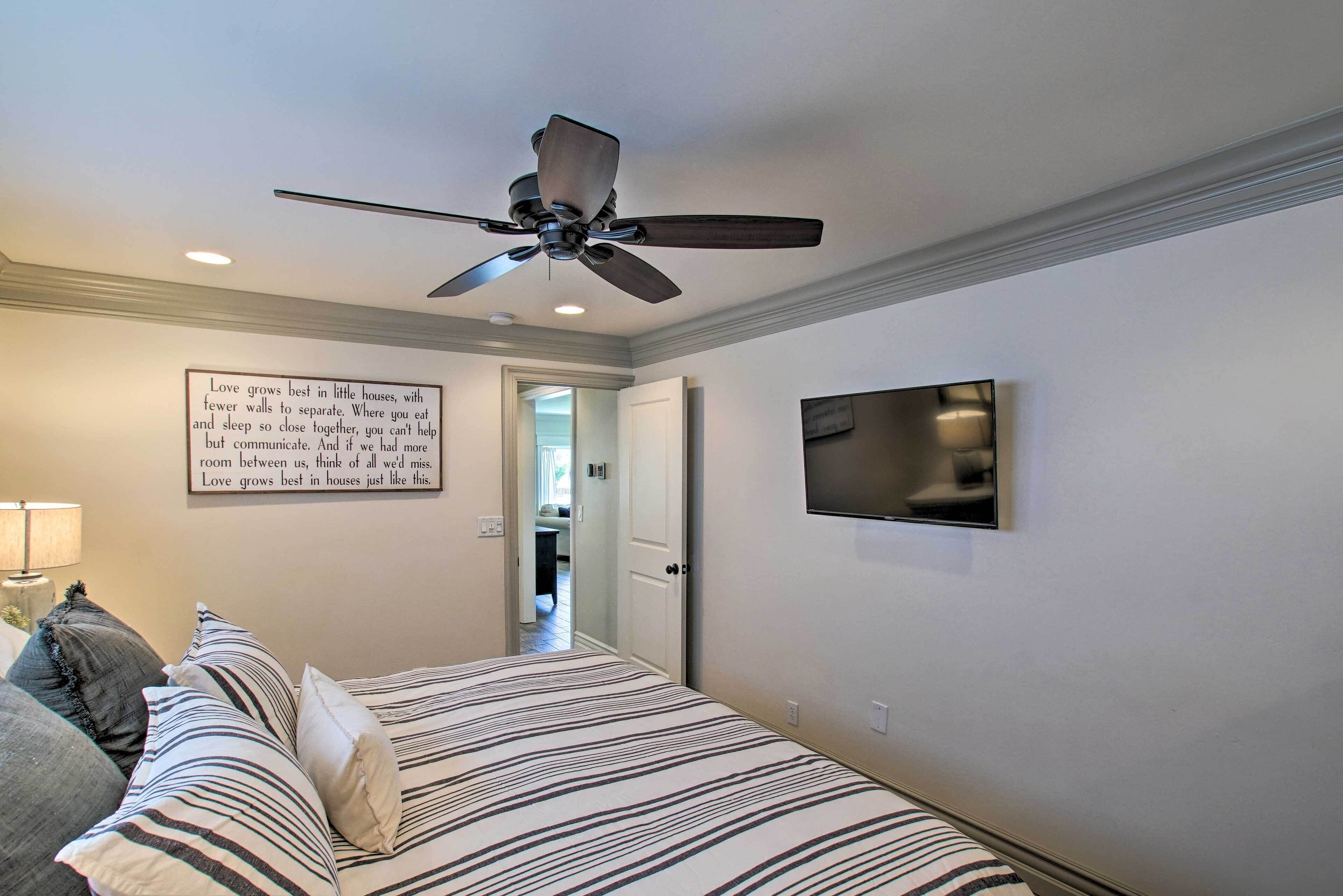 A bedroom with a bed, a ceiling fan, a television, and a motivational quote on the wall.