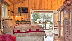 Camera da letto in una baita di legno, con un letto, una televisione, un armadietto in legno e un balcone con vista all'esterno.