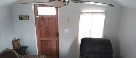 A room with a ceiling fan, a wooden door, a window with curtains, and a dark armchair.