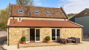 A stone house with a tiled roof, a patio with outdoor furniture, and a small garden. - Middle Barn - sleeps 6 guests  in 3 bedrooms (Chippenham)