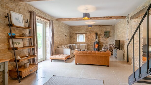 A cozy living room with a stone wall, a fireplace, a sofa, and a staircase. - Middle Barn - sleeps 6 guests  in 3 bedrooms (Chippenham)
