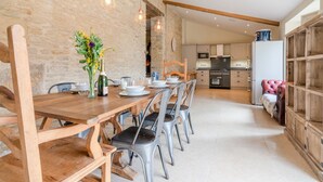 A dining area with a wooden table and chairs, a vase with flowers, and a kitchen in the background. - Middle Barn - sleeps 6 guests  in 3 bedrooms (Chippenham)