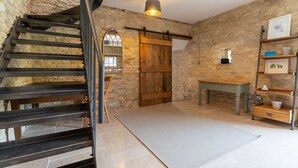 A rustic interior with a stone wall, a wooden staircase, a sliding barn door, a small wooden table, and a metal shelf with decorative items. - Middle Barn - sleeps 6 guests  in 3 bedrooms (Chippenham)