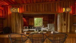 L’intérieur d’un chalet rustique en bois comprend un coin cuisine, une table à manger avec des chaises et une fenêtre qui laisse entrer la lumière naturelle.