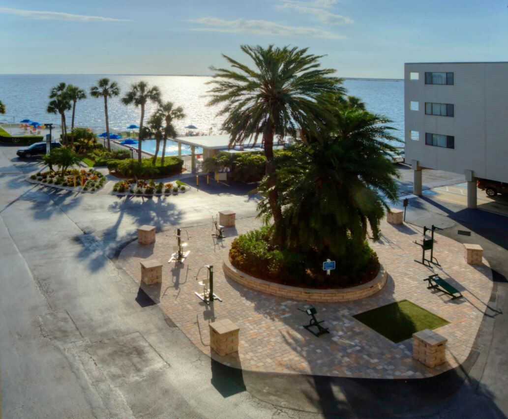 A courtyard with palm trees, a pool, and a beach view.