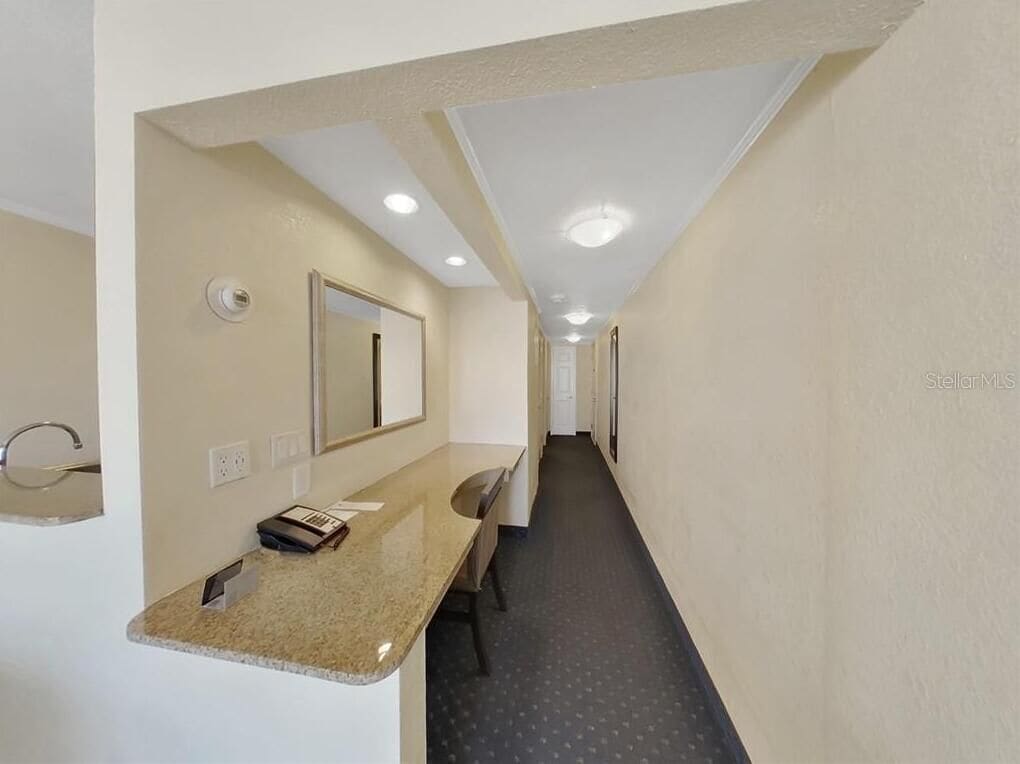 Un pasillo de hotel con un espejo, mostrador y una puerta al final.