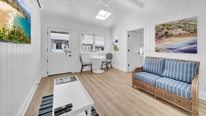 A spacious living area with a white ceiling, a ceiling fan, a large window, a wicker sofa, a dining table, and a kitchen area. - LOVELY DESIGNER COTTAGE!   3 MIN WALK TO THE BEACH AND HEISLER PARK! (Laguna Beach)