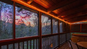 Eine Holzterrasse mit Blick auf Bäume und einen Sonnenuntergang.