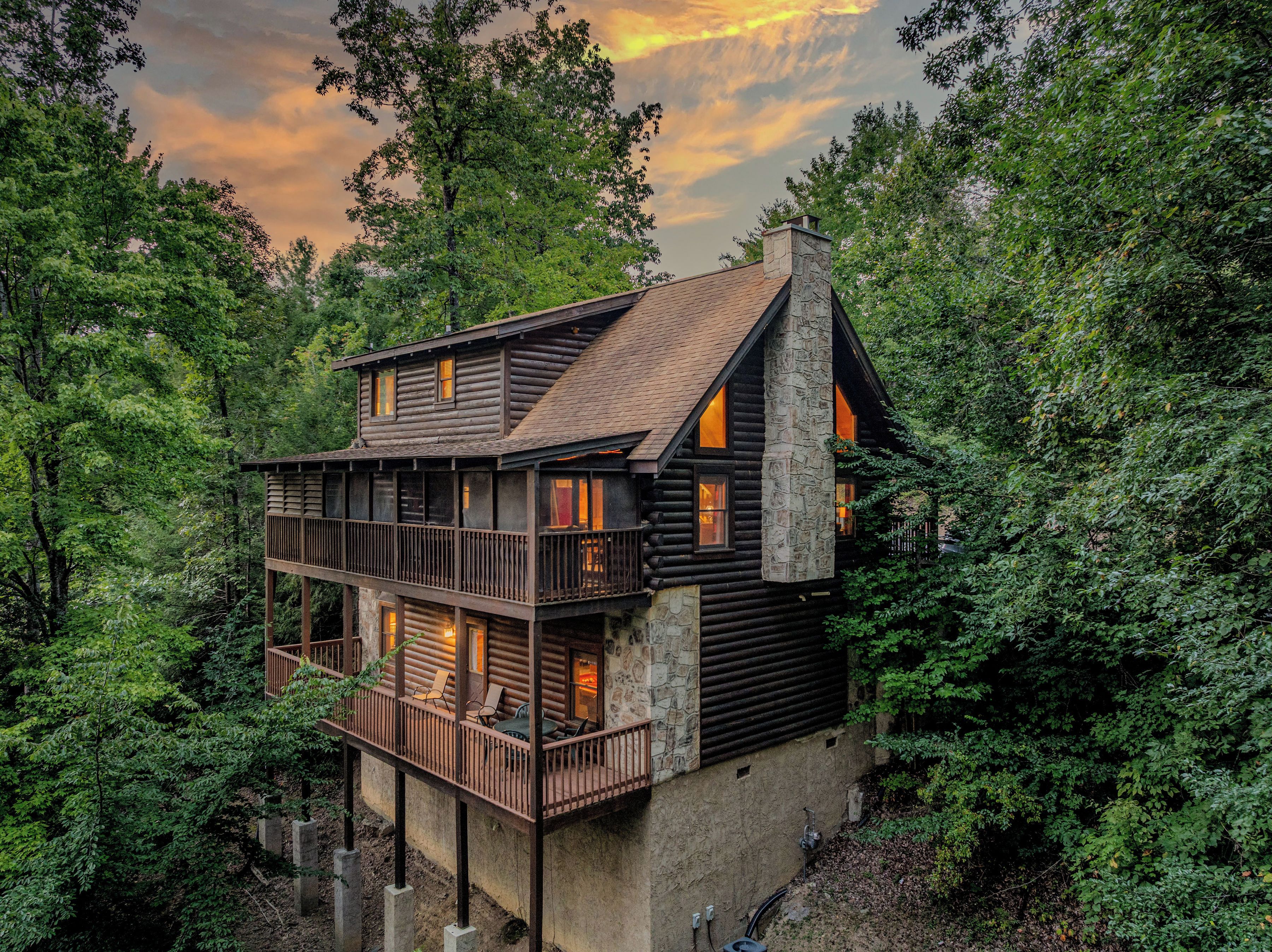 En timmerstuga med en balkong och en stenskorsten, omgiven av tät skog.