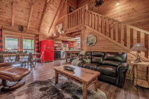 A cabin interior with a wooden staircase, a red refrigerator, a leather sofa, and a dining area.
