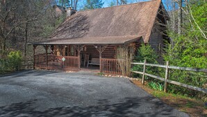 Ein rustikales Blockhaus mit Veranda, umgeben von Bäumen und einem Holzzaun.