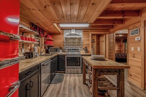 A compact kitchen with wooden walls, a red refrigerator, and stainless steel appliances.