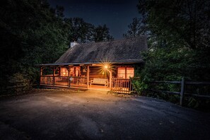 A log cabin with a porch, a visible cabin sign, and a gravel driveway.
