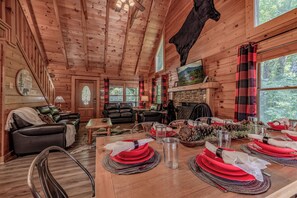 L’intérieur d’une cabane comprend une table à manger dressée pour quatre personnes, une cheminée, des canapés en cuir et un grand plafond en bois.