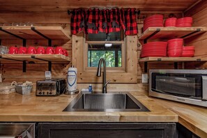 A kitchen with a stainless steel sink, a toaster, a microwave, and shelves with red dishes. - Updated^Step-Free Access^EZMobility^KingSuite^2m to Parkwy^EZRoads^FastWiFi (Pigeon Forge)