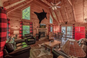 A cozy cabin interior with a fireplace, leather furniture, and a ceiling-mounted animal sculpture.