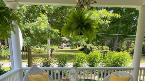 A covered outdoor seating area with wicker chairs and a glass table, surrounded by a patterned rug and white columns. - Charming Lakeside cottage , will sleep 10 (Bemus Point)