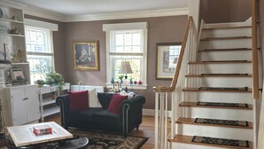 A living room with a staircase, a black sofa, a coffee table, and a dog. - Charming Lakeside cottage , will sleep 10 (Bemus Point)