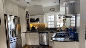 A modern kitchen with stainless steel appliances, white cabinetry, a gas stove, and a large window providing natural light. - Charming Lakeside cottage , will sleep 10 (Bemus Point)