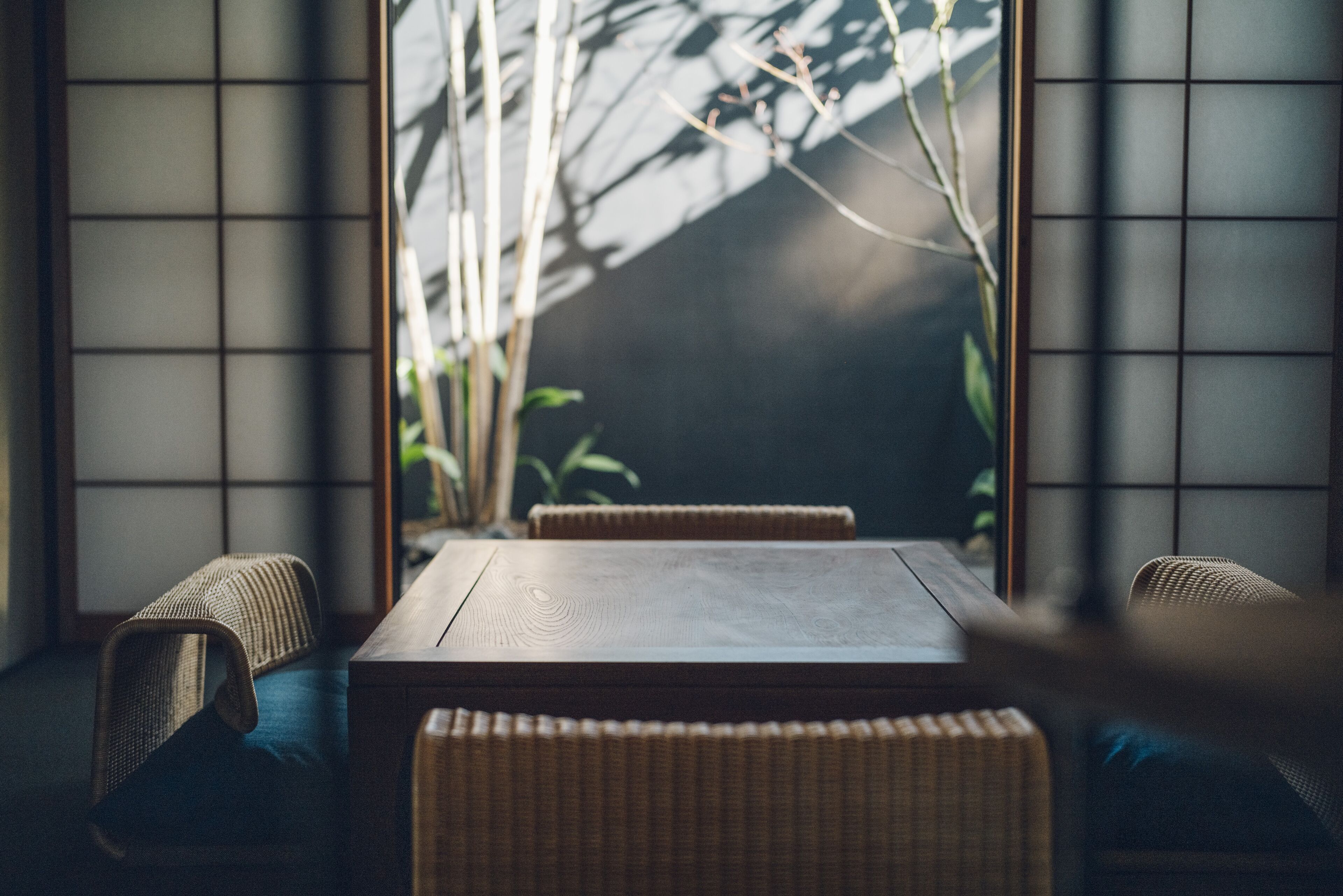 A traditional Japanese room with tatami flooring, a low wooden table, and a view of bamboo outside.