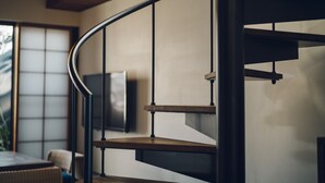 Moderni sisustus, jossa on kaarevat portaat, seinälle asennettu taulutelevisio ja taustalla perinteinen japanilainen liukuovi.