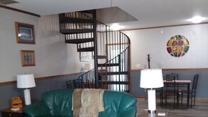 A living room with a green sofa, a wooden coffee table, a spiral staircase, and a dining area with a table and chairs. - Peaceful retreat for all seasons' (Beaver Dam)