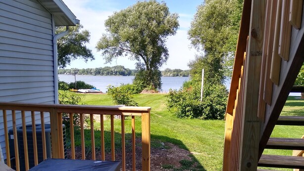 A wooden deck with a covered grill area, leading to a grassy yard with trees and a lake view. - Peaceful retreat for all seasons' (Beaver Dam)