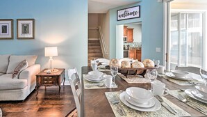 Un coin repas avec une table en bois dressée pour quatre personnes, un canapé et un escalier menant à un niveau supérieur.