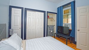 Une chambre à coucher avec un lit, un téléviseur posé sur un meuble, une armoire et une porte avec une fenêtre.