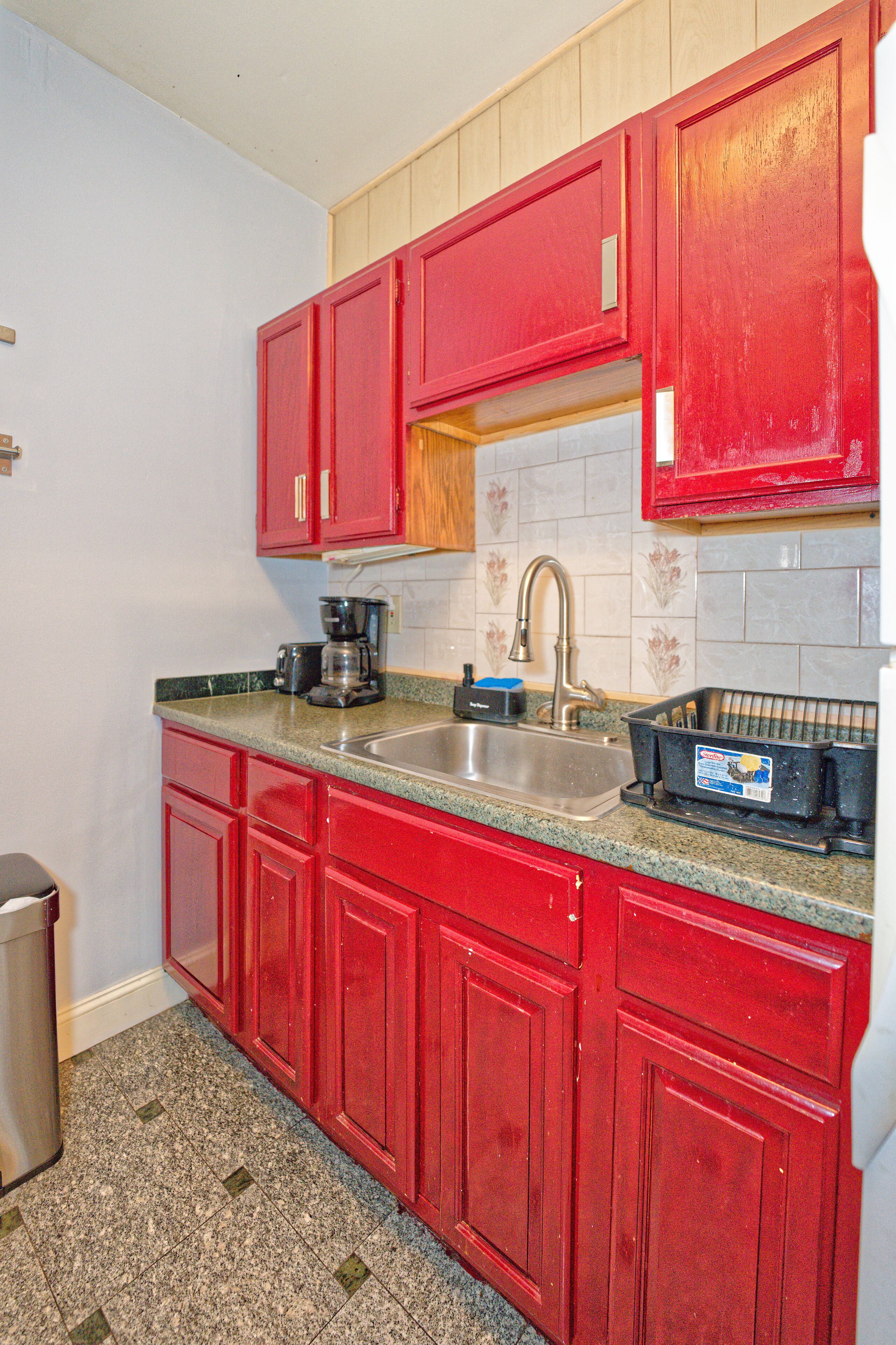 A kitchen with red cabinets, a stainless steel sink, and a coffee maker.