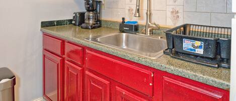 A kitchen with red cabinets, a stainless steel sink, and a coffee maker.