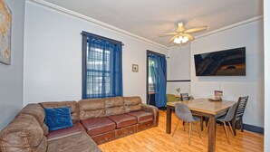 Un salon avec un canapé en cuir marron, une table à manger en bois avec des chaises et un ventilateur de plafond.