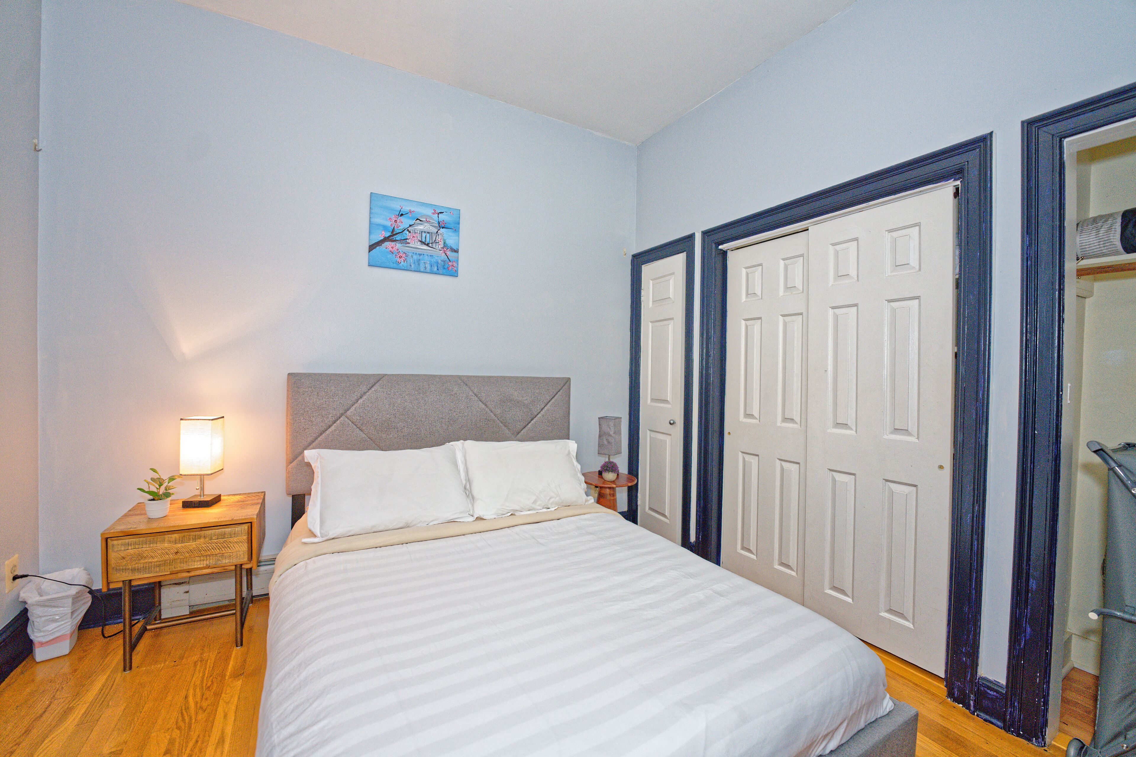 A bedroom with a bed, bedside table, lamp, and a door.