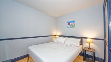 A bedroom with a bed, a nightstand with a lamp, a small painting on the wall, and wooden flooring.