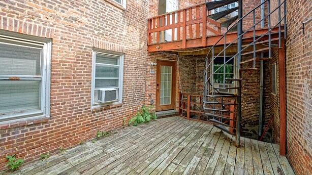 Un bâtiment en briques avec une terrasse en bois, une porte et un escalier en métal.