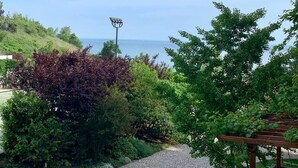 Ein gepflasterter Weg führt zu einem Pergola mit Blick auf ein Gewässer, umgeben von üppiger Vegetation.