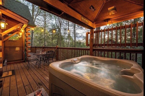 Relax on the deck with a hot tub and outdoor seating area amidst a serene wooded setting.