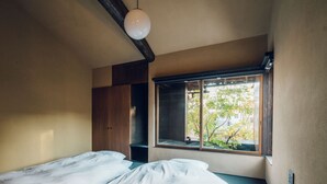 Un dormitorio con cama, armario y ventana con vistas a árboles y edificios.