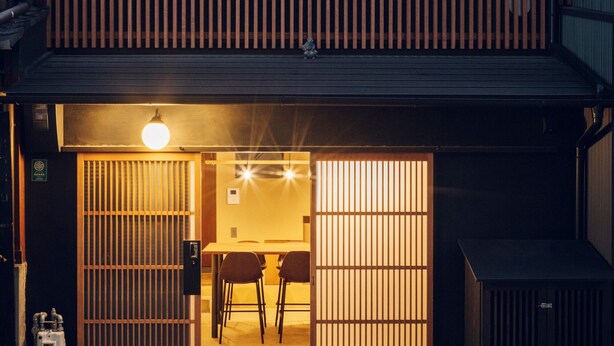 Una entrada de estilo japonés tradicional con puertas correderas, un pequeño comedor con mesa y sillas, y una lámpara colgante.