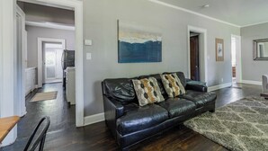 A living room with a black leather sofa, a rug, and a painting on the wall.