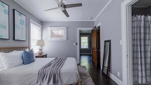 A bedroom with a bed, a ceiling fan, framed pictures, and a window.