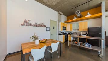 A modern kitchen with a wooden dining table, white chairs, and a kitchen island with appliances.