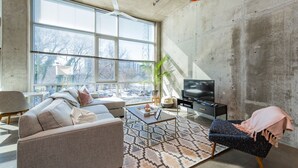 Una sala de estar moderna con un ventanal grande, un sofá, una mesa de centro, un televisor y una planta.