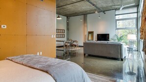 A modern hotel room with a large bed, a sofa, a TV, and a dining area with a table and chairs. - Stylish Gulch Loft Close to Downtown Broadway (Nashville)