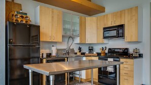 A modern kitchen with wooden cabinets, stainless steel appliances, and a central island. - Stylish Gulch Loft Close to Downtown Broadway (Nashville)