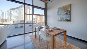 Zona menjador moderna amb un finestral gran, taula de fusta, cadires blanques i vista a la ciutat.