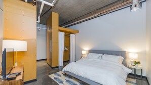 Una habitació d'hotel moderna amb un llit gran, una taula de treball amb un ordinador i un bany amb cortina de dutxa.